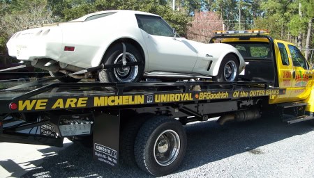 Classic white sports car being loaded onto a tow truck for repair or transport.
