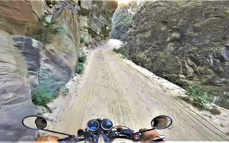 Motorcycle riding through narrow rocky canyon on Sach Pass trail.