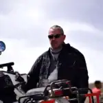 Rider in black gear with motorcycle on scenic outdoor trail.