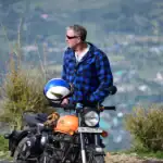 Motorcycle rider with helmet and gear in scenic outdoor setting.