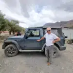 Man standing next to a rugged off-road vehicle in desert landscape.