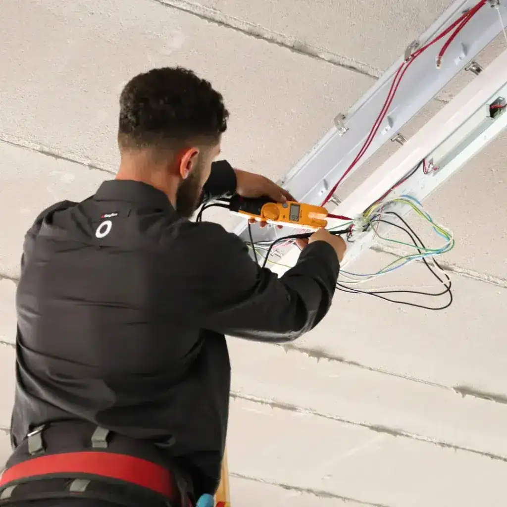 Electrician performing maintenance on commercial electrical wiring, using a multimeter to ensure safety and functionality in a business setting.