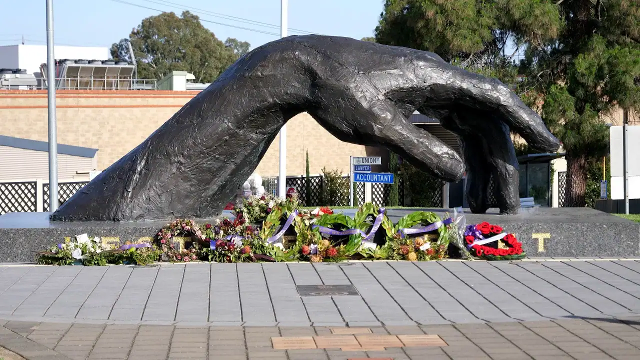 Large bronze hand sculpture with floral tributes at its base, located in Gawler, symbolising community and remembrance for local electrical services.