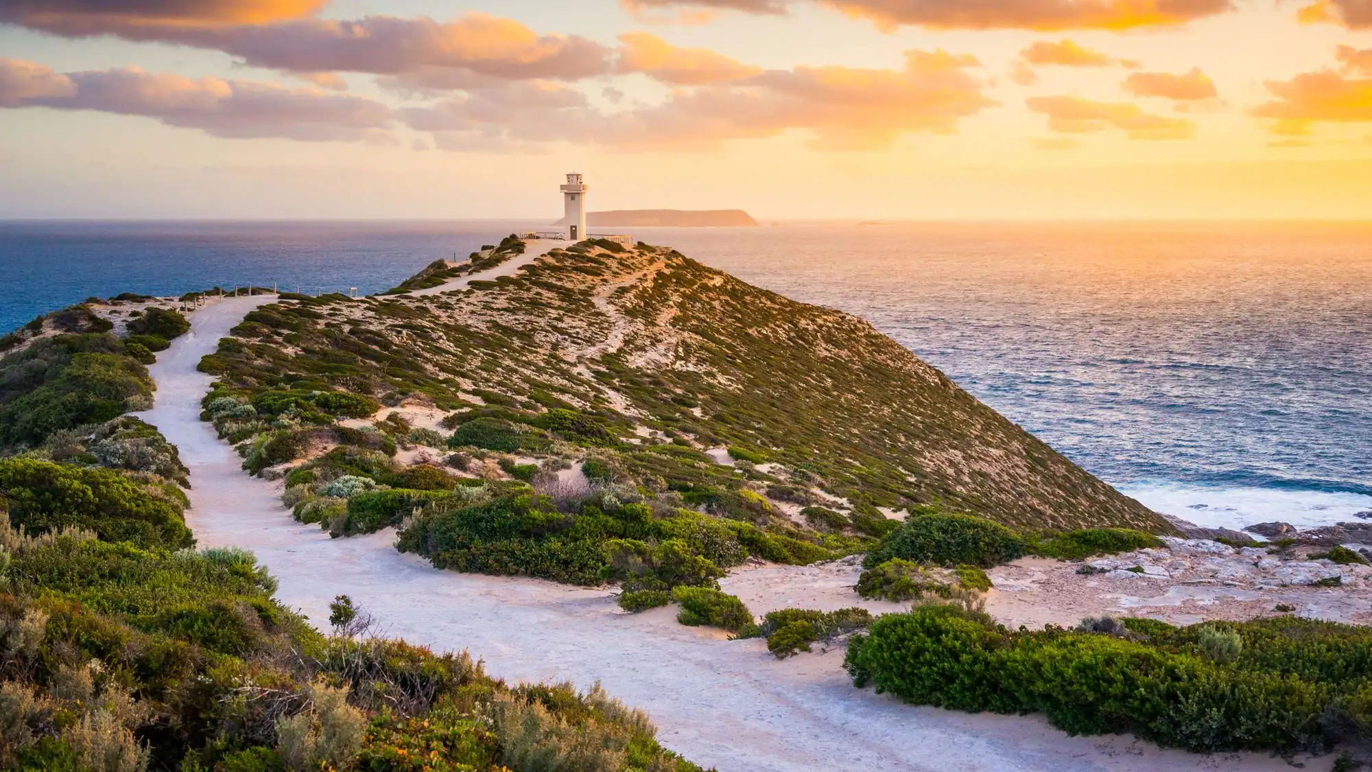 Coastal landscape featuring a winding path leading to a lighthouse on a hill, overlooking the ocean at sunset, with lush greenery in the foreground, relevant to Ozora's reliable electrical services in Marion.