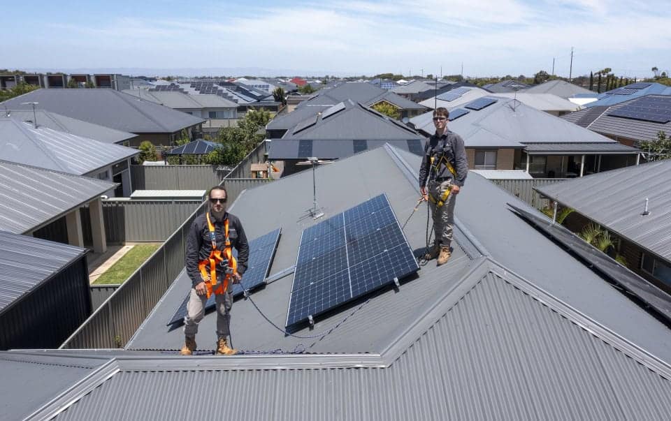 Two technicians installing solar panels on a residential roof in Mildura, showcasing solar energy solutions amidst a neighbourhood with multiple solar installations.