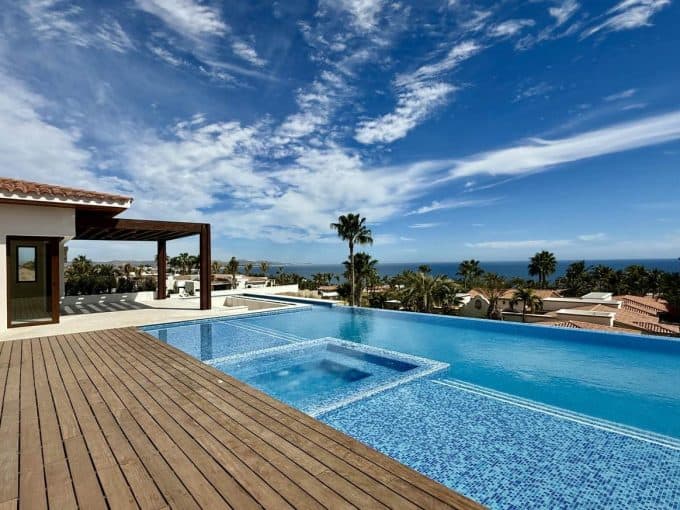 A Pool With A Deck And A Wood Deck With A Wood Deck And A Blue Sky With Clouds