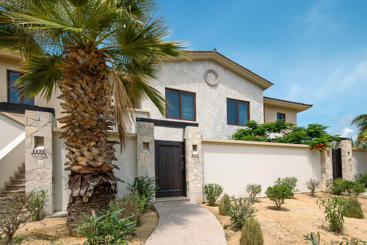 Luxurious Palmilla Home With A Modern Exterior, Surrounded By Tropical Landscaping Including Palm Trees And Shrubs, Showcasing Coastal Elegance And Privacy In A Gated Community.