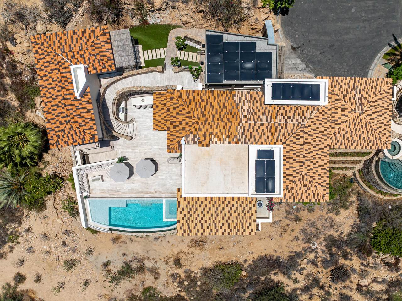Modern Palmilla Home With Tiled Roof, Outdoor Pool, Terrace With Umbrellas, Solar Panels, Lush Landscaping, And Scenic Desert Views In A Luxurious Desert Community.