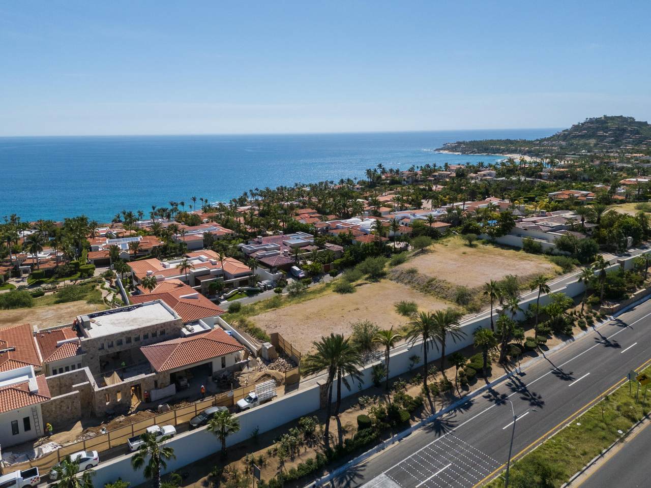 Aerial View Of Palmilla Coastal Neighborhood With Ocean In Background, Featuring Houses With Red Tile Roofs And Lush Greenery Along A Main Road.