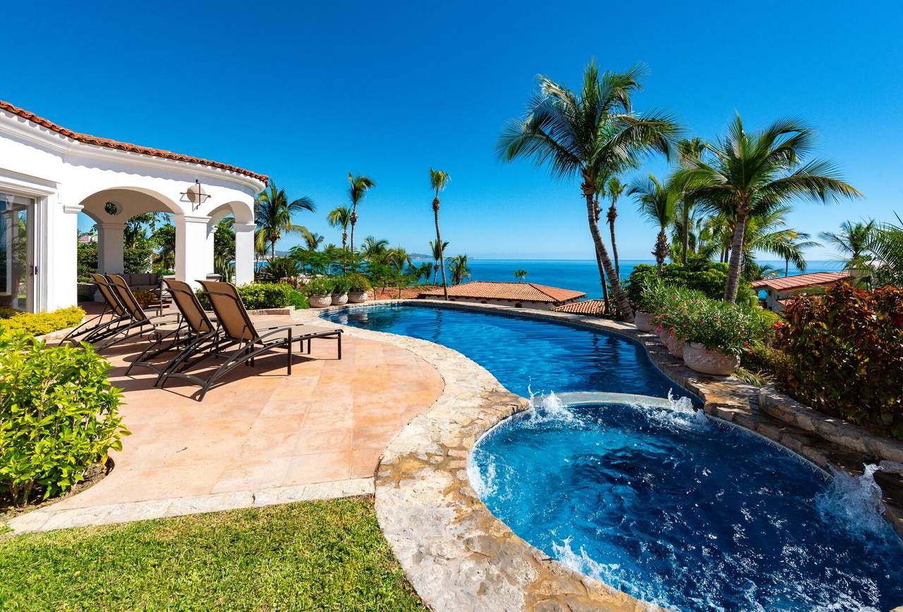 Luxurious Palmilla Ocean View Poolside Patio With Lounge Chairs, Lush Tropical Plants, And Palm Trees, Offering Stunning Ocean Vistas And A Perfect Relaxing Retreat.