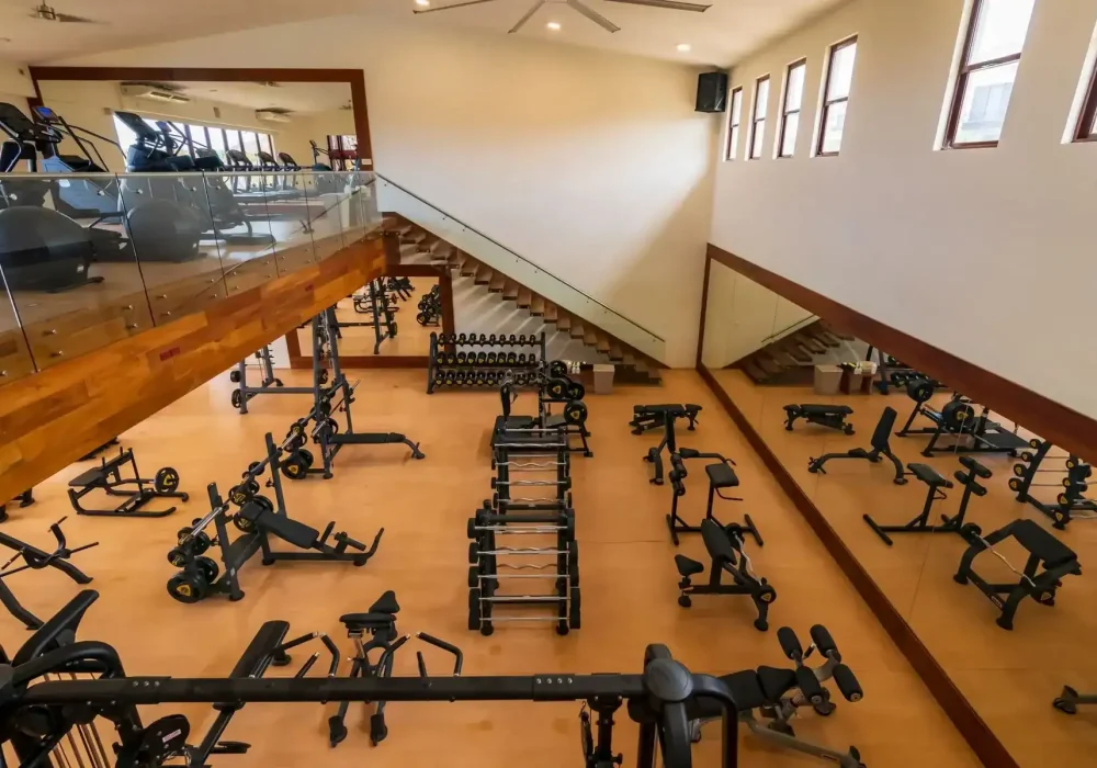 Fitness And Wellness – Homes For Sale In Palmilla Spacious Palmilla Fitness Center Featuring Modern Cardio Equipment And Free Weights, With Large Windows Providing Natural Light And A Mirrored Wall For Workouts.