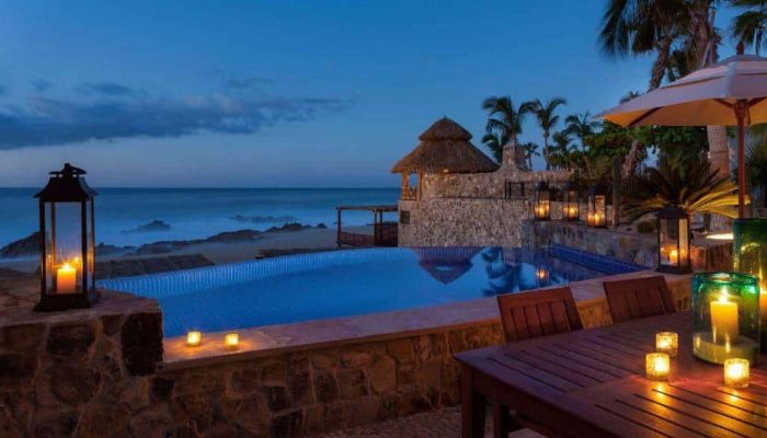 Luxurious Palmilla Beachfront Poolside Scene Illuminated By Candles At Dusk, Showcasing Ocean Views, Tropical Plants, And Cozy Seating Areas. Perfect For Palmilla Real Estate Admiration And Seaside Relaxation.