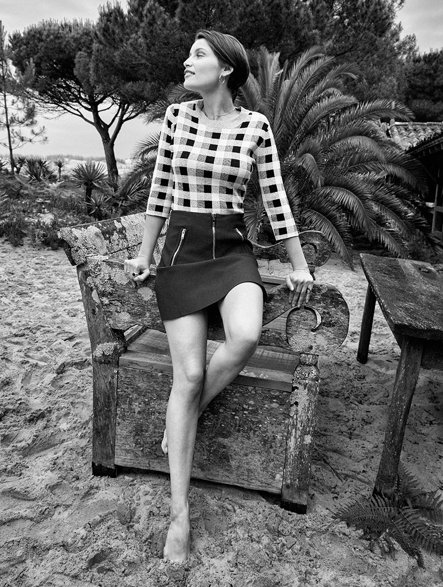 Elegant black and white portrait of a woman sitting on a rustic wooden bench in a tropical outdoor setting, showcasing professional fashion photography by Pamela Hanson.