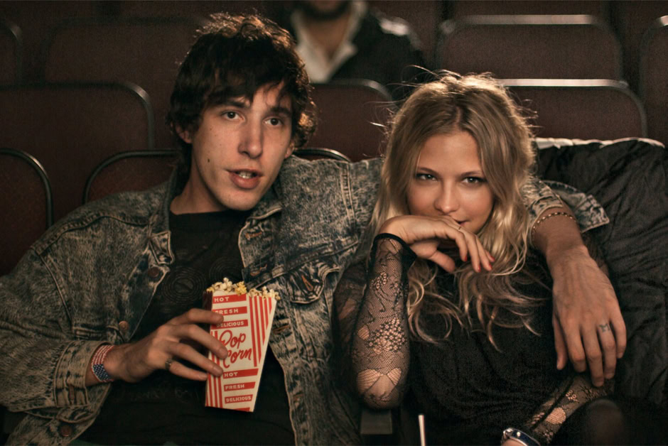 Young couple enjoying a movie at the cinema, with the man holding a bucket of popcorn, showcasing candid moments, romantic vibe, and entertainment lifestyle photography.