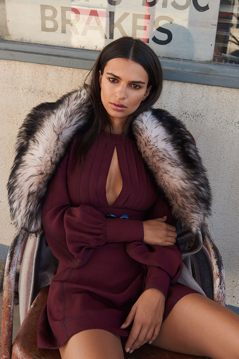 A woman in a stylish maroon dress with a fur coat sitting on a vintage chair outdoors.