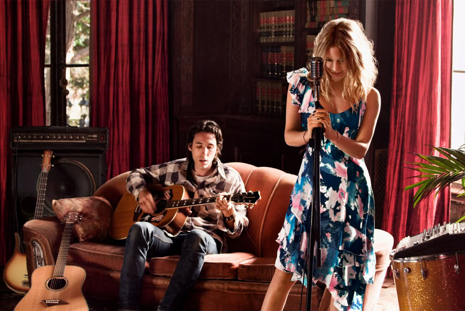 Guitarist and singer performing live session in vintage-inspired indoor setting with red curtains, musical instruments, and warm natural light, capturing artistic musical performance.