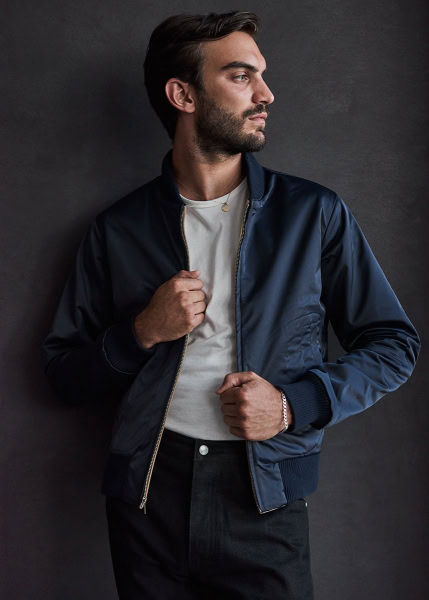 Elegant male model wearing a navy bomber jacket and white T-shirt, styled for a fashion photography shoot by Pamela Hanson, showcasing modern men's fashion and portrait photography.