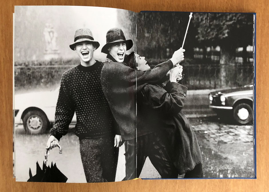 Vibrant street style portrait of three women enjoying a rainy day, capturing genuine joy and friendship, with vintage cars in the background. Black and white photography emphasizing textures and expressions.
