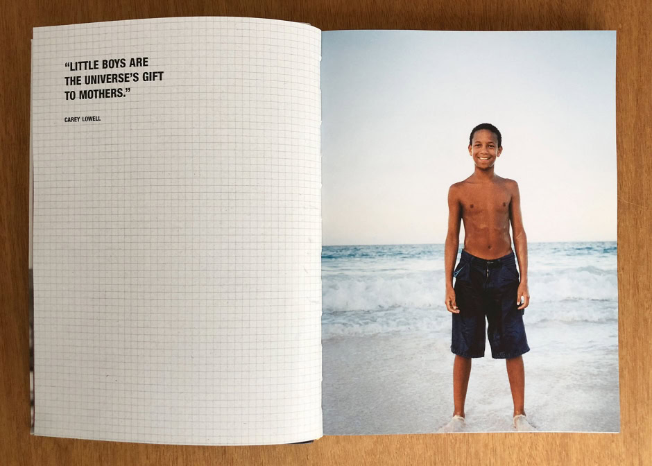Vibrant beach portrait of a smiling young boy shirtless in navy shorts, standing on sand near ocean waves under clear sky, captured by Pamela Hanson Photography for timeless seaside imagery.