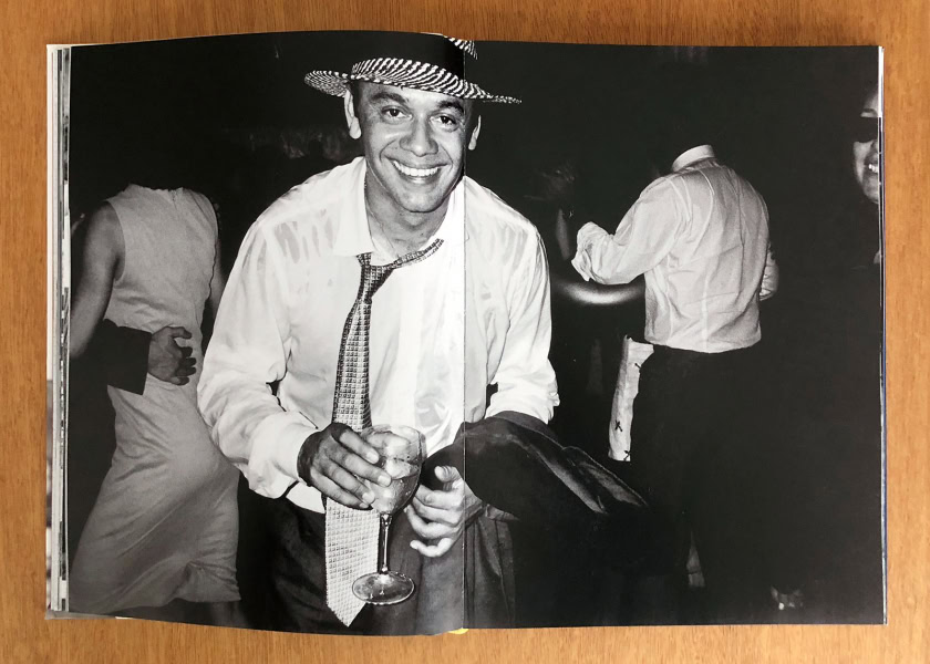 Elegant black and white photograph of a smiling man wearing a hat, tie, and dress shirt holding a drink, capturing a lively moment at a social event or party.