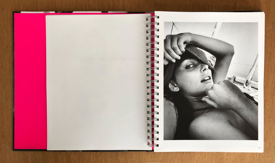 Black and white portrait of a woman with intense gaze, holding a hat over her eye and posing with her hand near her chin, showcasing elegant and artistic fashion photography.