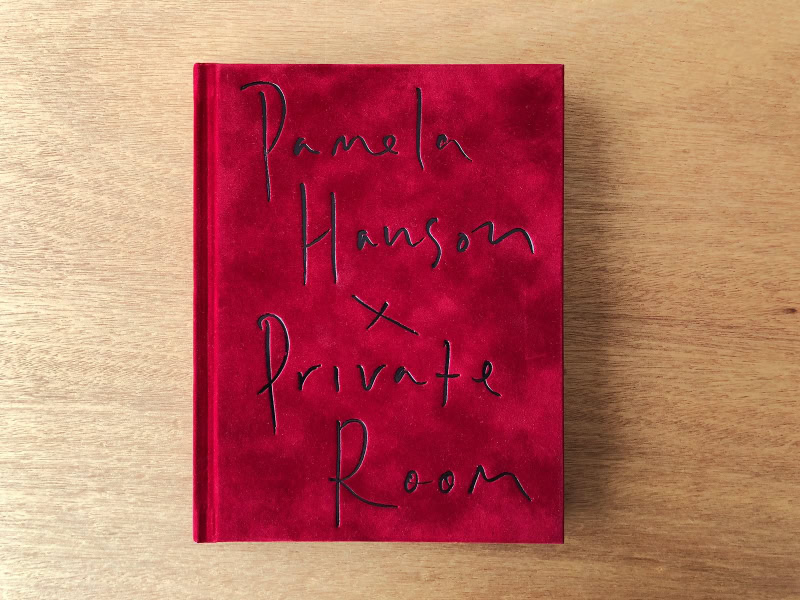 A red hardcover book titled “Palms Hanson x Private Room” resting on a light wooden surface.