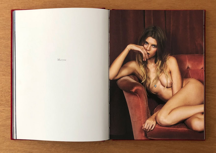 Elegant portrait of a nude woman with wavy hair, seated on a vintage red velvet sofa, captured by Pamela Hanson Photography.
