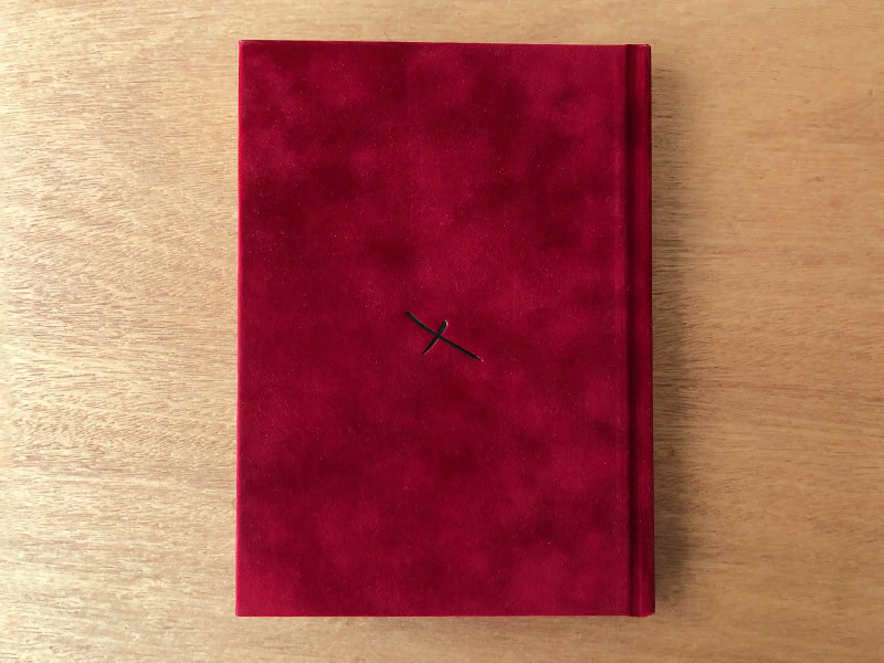 Elegant red hardcover book on wooden surface, minimalist design, possible journal or poetry book, sophisticated aesthetic, high-quality photography.