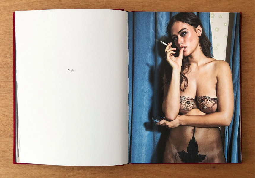 Elegant portrait of a woman with dark hair holding a cigarette, wearing delicate floral lace lingerie, against blue curtains; high-quality fashion photography by Pamela Hanson.