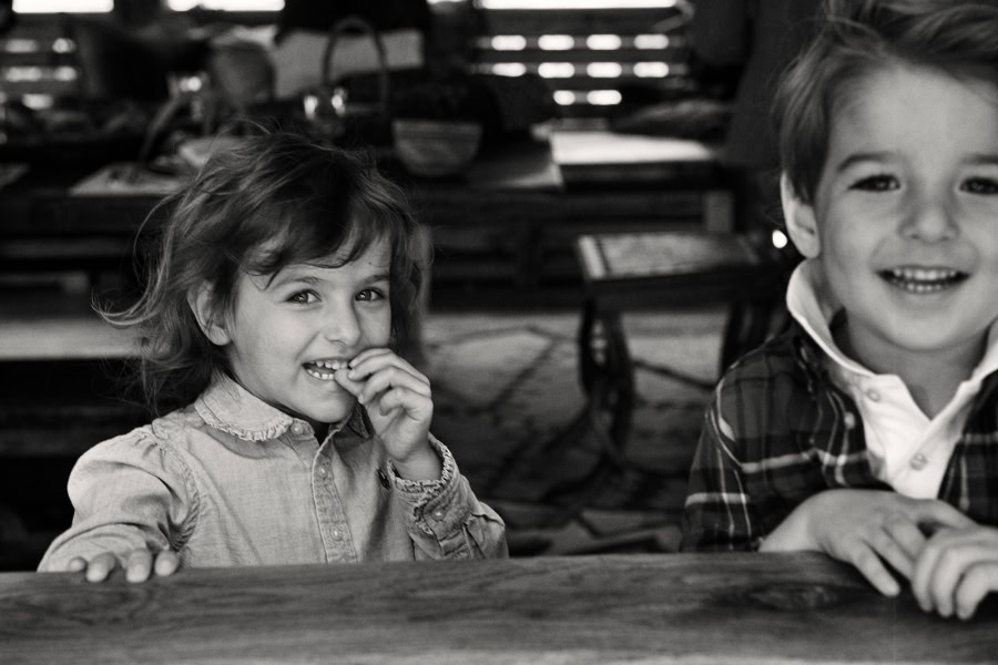 Children laughing and smiling indoors, black and white photography, candid portrait shot capturing childhood joy, family moments, authentic expressions, artistic black and white portrait.