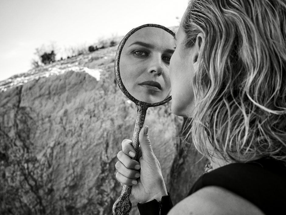 Mirror reflection of woman's face, black and white photography, outdoor portrait, artistic beauty shot, model with wet hair, natural surroundings, high-resolution fashion photography, emotional expression, Pamela Hanson Photography relevance.