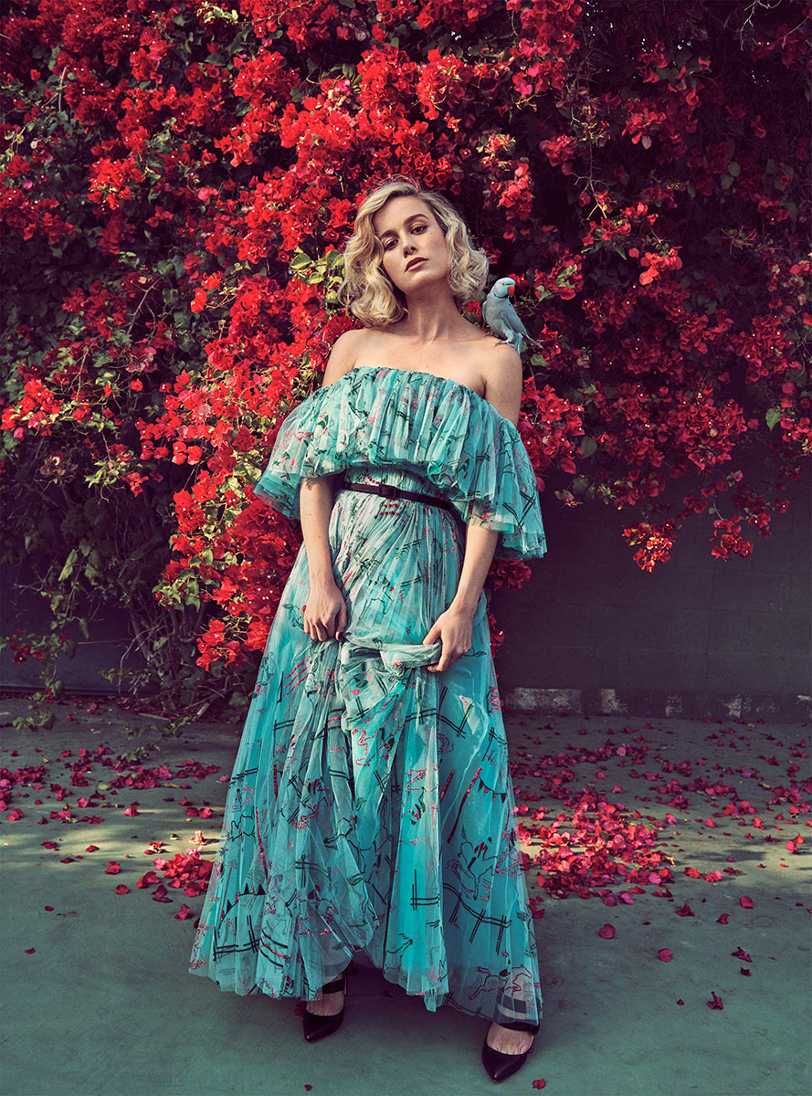 Vogue-inspired fashion portrait of a glamorous woman in an elegant turquoise dress with bold brushstroke patterns, standing against a lush red bougainvillea backdrop, accented by a colorful parrot perched on her shoulder, showcasing high-end fashion photography.