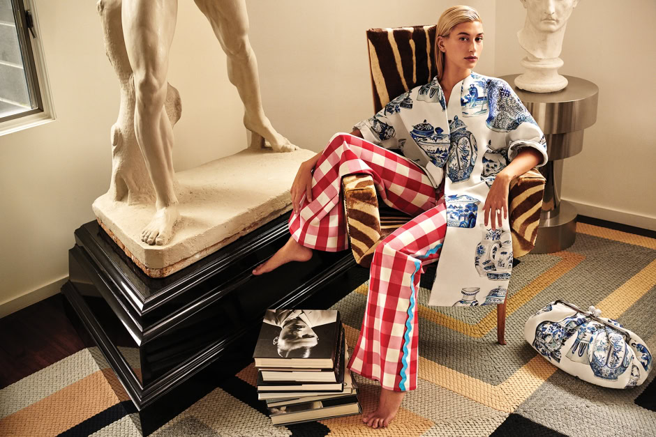 Elegant woman sitting on a striped armchair in an art gallery, surrounded by classical sculptures and art books, showcasing Pamela Hanson photography style.