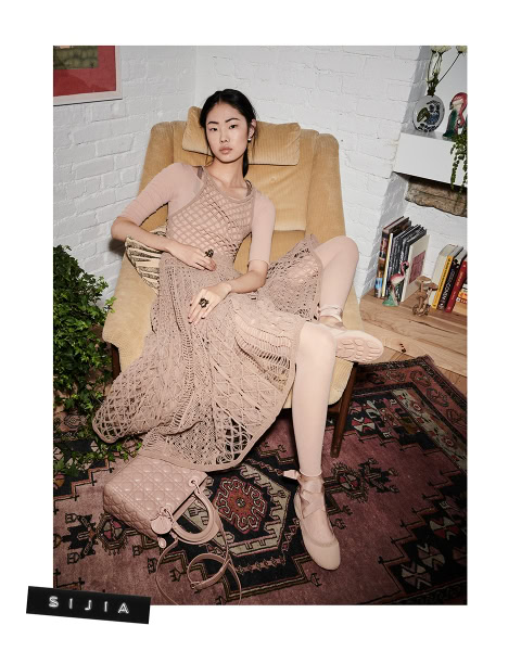 Elegant fashion portrait of an Asian female model relaxing on a beige armchair, showcasing intricate knitwear and accessories in a cozy, stylish interior.