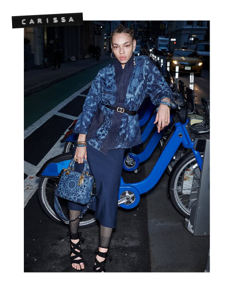 Elegant city street fashion shoot featuring a woman in a chic blue ensemble with designer accessories, urban backdrop, and bike-sharing station. Perfect for high-end street style and fashion photography.