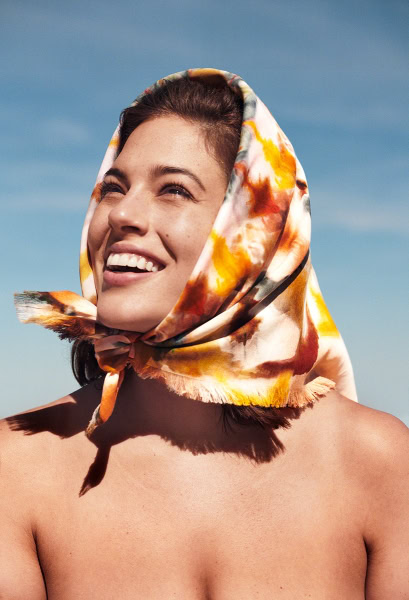 Vibrant portrait of a smiling woman with a floral scarf against a clear blue sky, showcasing natural beauty and fashion photography skills.