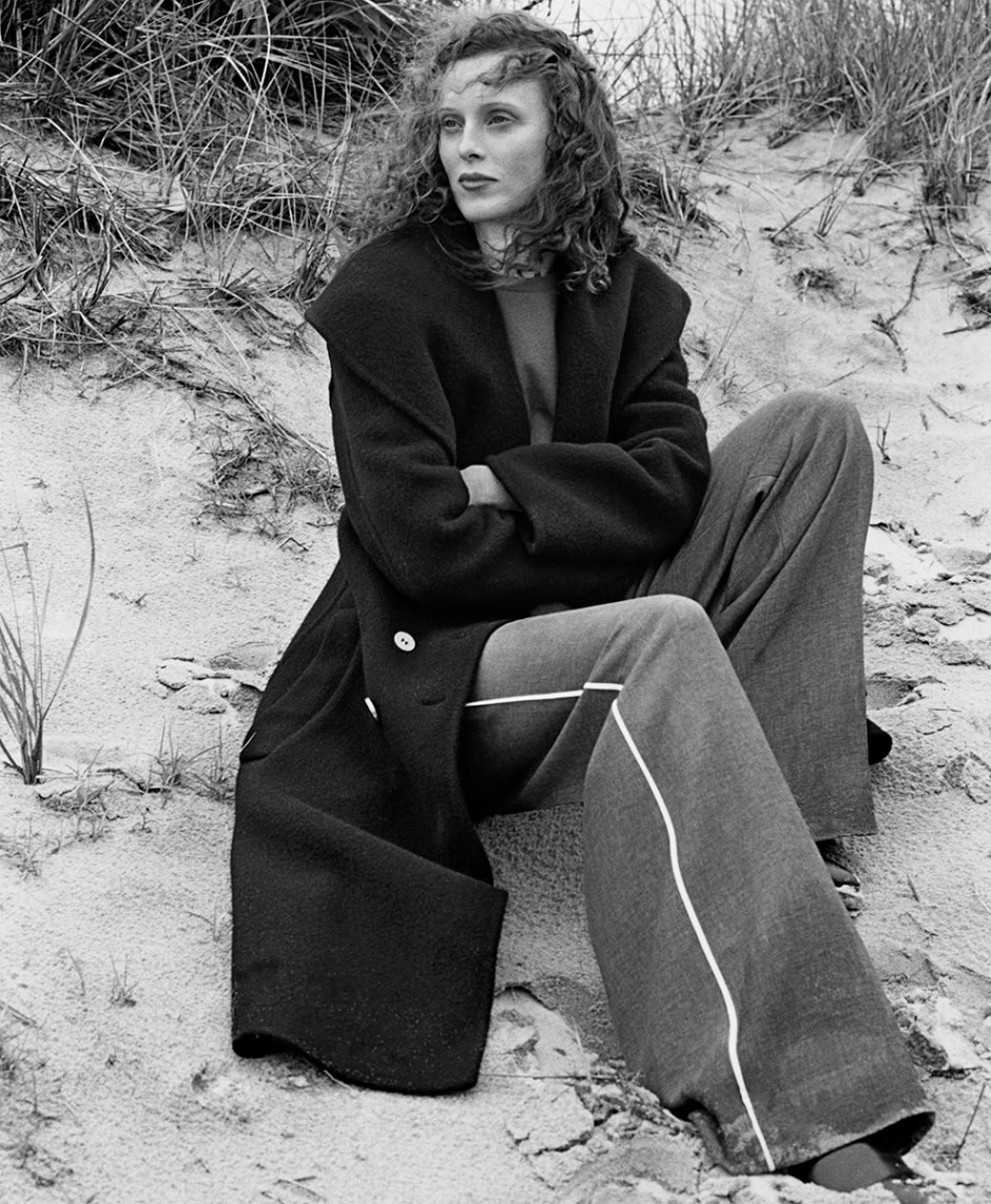 Soft black and white portrait of a woman sitting on sandy dunes with tall grasses, showcasing natural beauty and fashion photography by Pamela Hanson.