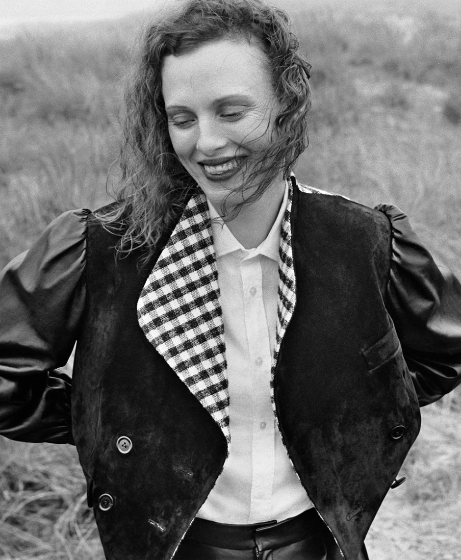 Black and white portrait of woman smiling outdoors, fashion photography by Pamela Hanson, stylish clothing and natural expression, depth of field with blurred natural background, editorial and lifestyle shot, professional female model, high-quality photography, timeless black-and-white photography, elegant and candid imagery, female portrait photography, natural lighting and authentic emotion.