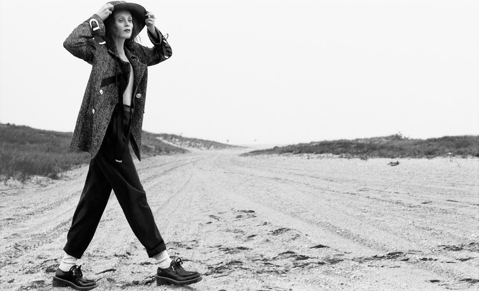 Elegant fashion portrait of a woman standing on a sandy beach, modeling trendy clothing and accessories, captured by Pamela Hanson Photography, showcasing her signature style and landscape photography expertise.