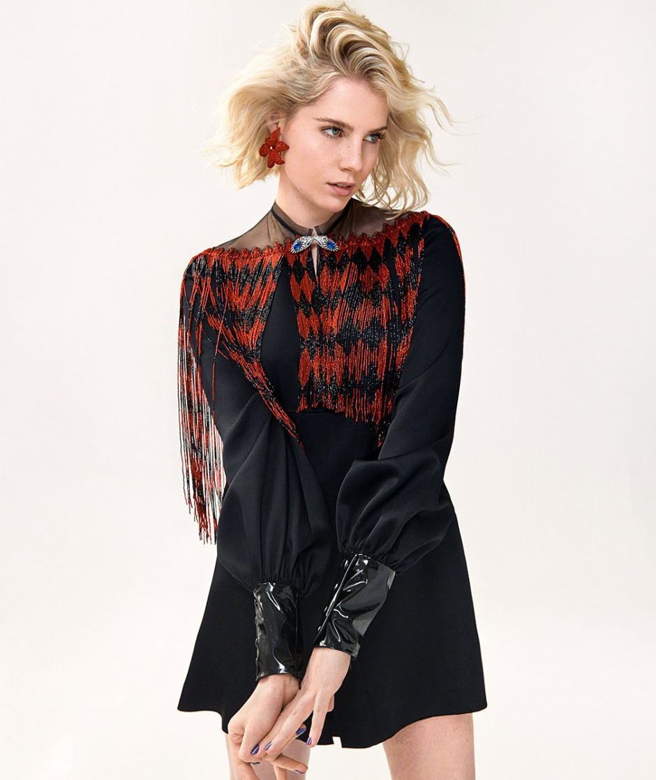 Elegant fashion portrait of a blonde female model wearing a black dress with red and black embroidered accents, featuring lace and fringe details, captured by Pamela Hanson Photography.