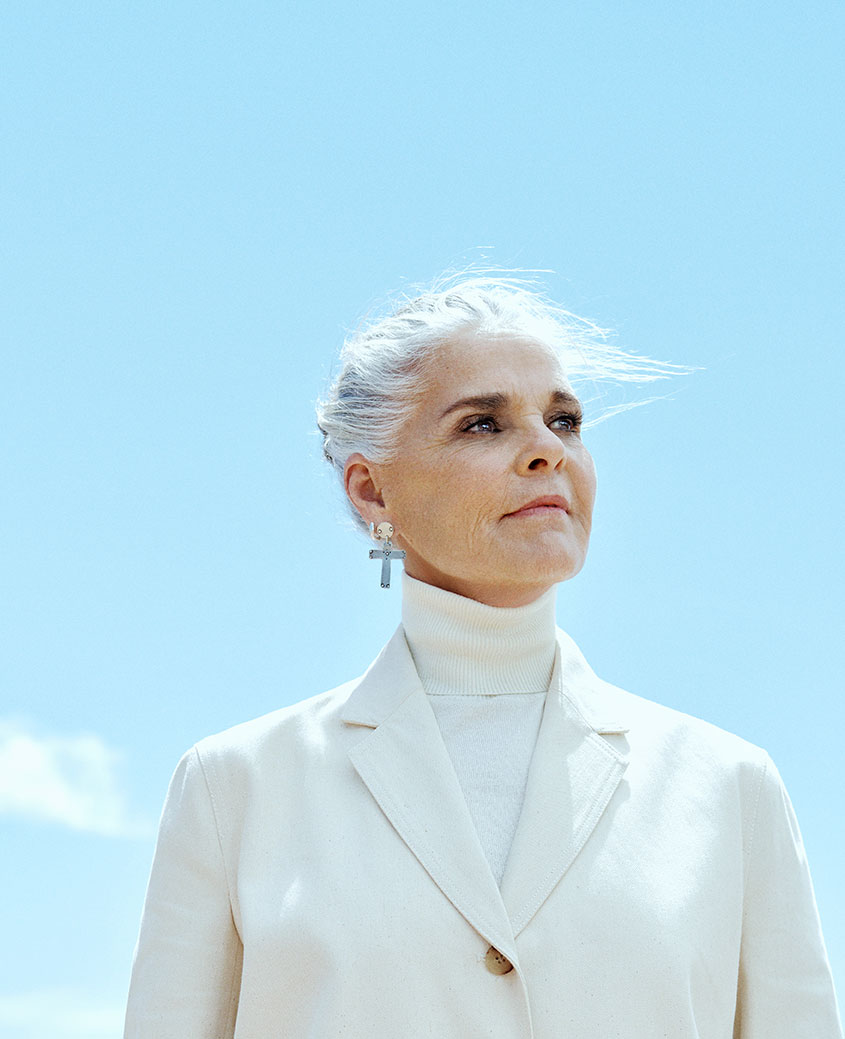Elegant portrait of an older woman with silver hair wearing a white blazer and turtleneck against a clear blue sky, showcasing fine art fashion photography by Pamela Hanson.