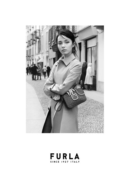 Elegant black and white street fashion portrait of a woman wearing a trench coat, holding a designer handbag, amidst a European cityscape, captured by Pamela Hanson Photography.