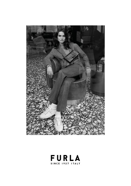 Elegant black and white fashion portrait of a young woman in tailored suit with sneakers, sitting confidently on a modern chair at a stylish café, showcasing luxury lifestyle and contemporary fashion photography.