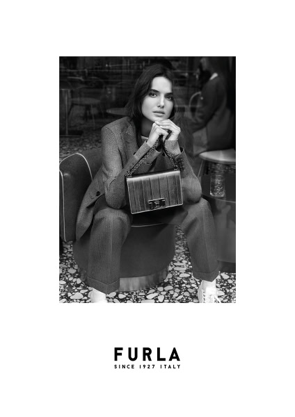 Elegant black and white fashion portrait of a woman in a tailored suit holding a luxury Furla handbag, showcasing sophisticated style and high-end accessories.