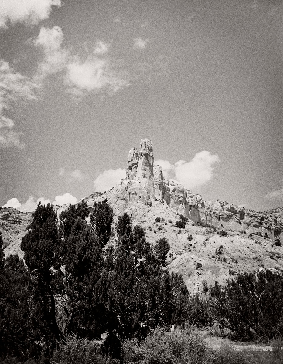 Majestic rock formation in black and white, surrounded by rugged desert landscape and sparse shrubbery, exemplifying dramatic nature photography by Pamela Hanson.