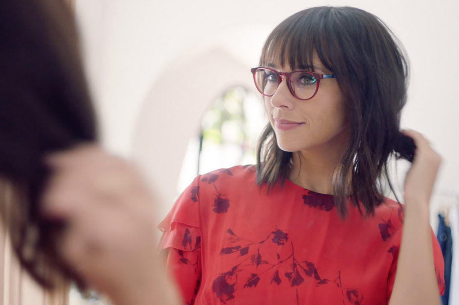 Elegant woman with shoulder-length dark hair, red glasses, and a stylish red floral blouse, engaging in a conversation. Photographed by Pamela Hanson, showcasing portrait photography, fashion, and lifestyle imagery.