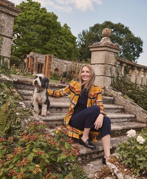 Elegant outdoor portrait of a woman with a dog on stone steps in a lush garden, showcasing professional portrait photography and nature-inspired settings, aligned with Pamela Hanson Photography’s style.