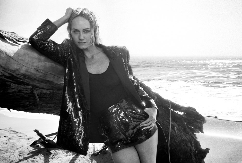 Elegant female model posing on a beach with driftwood, black sequin skirt, and leather jacket, showcasing high-fashion beachwear photography by Pamela Hanson.