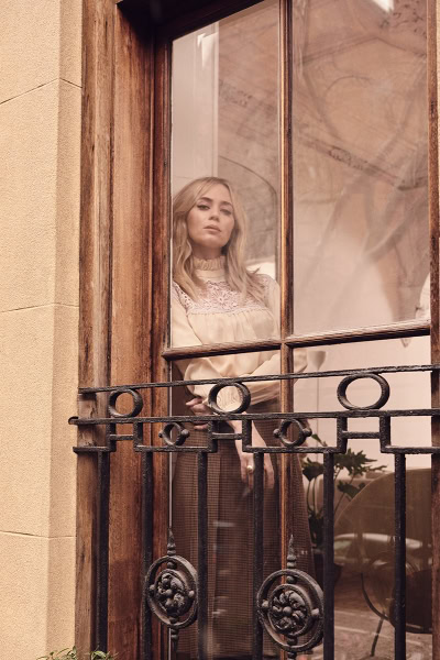Elegant woman looking through a window with vintage architectural details, capturing fashion photography and lifestyle aesthetics.