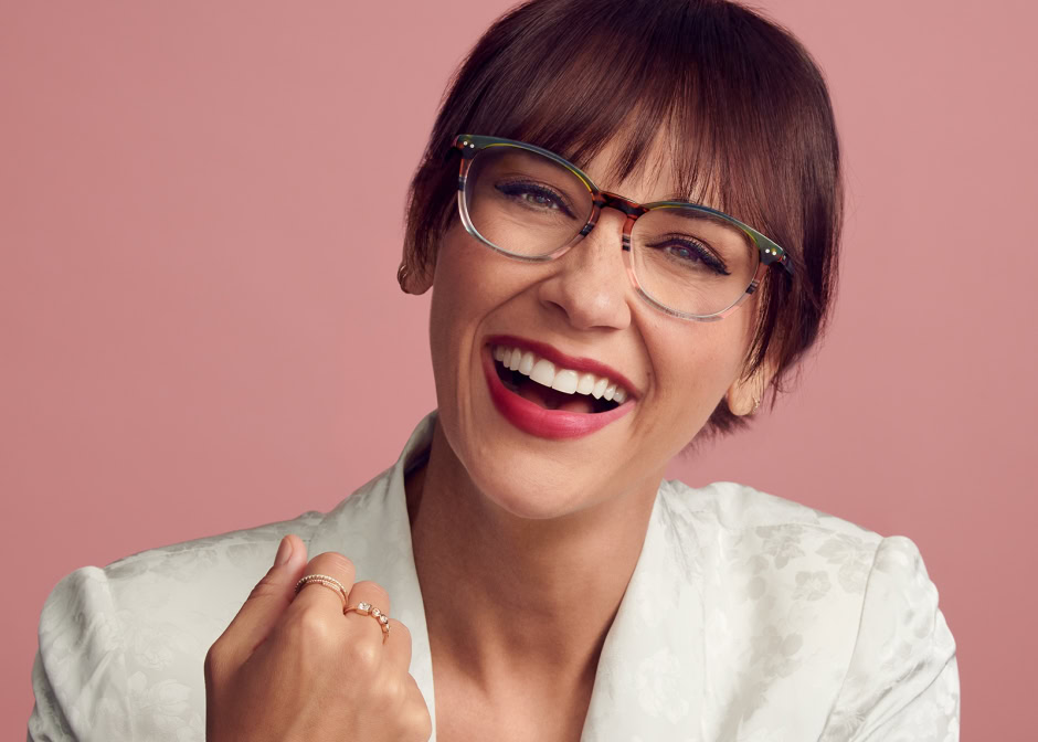 Bright smiling woman with short brown hair, glasses, and red lipstick, showcasing contemporary fashion and joyful expression in professional portrait photography.